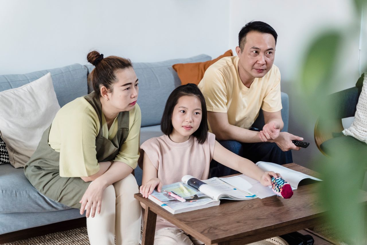 A family of three spending quality time indoors, seated on a couch with books and a remote.
